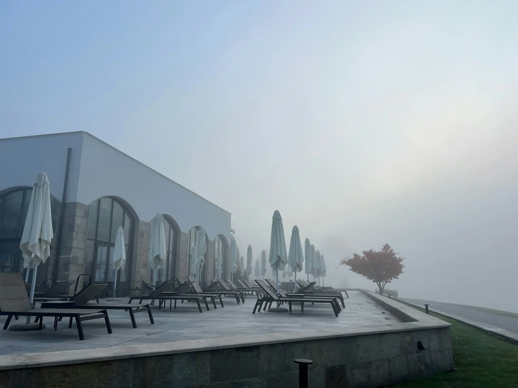 Empty sun loungers and closed umbrellas on a hotel terrace in morning fog